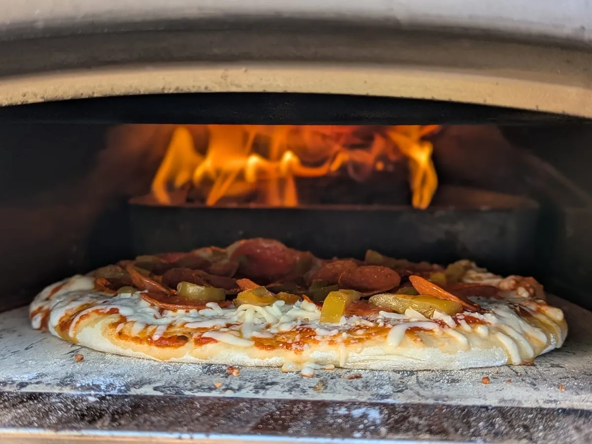 Pizza baking over an open flame in a wood-fired oven